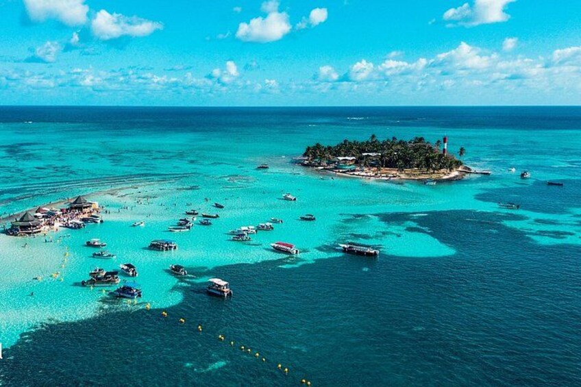 A turquoise sea with boats, a small island with a lighthouse, and a beach with structures. 5