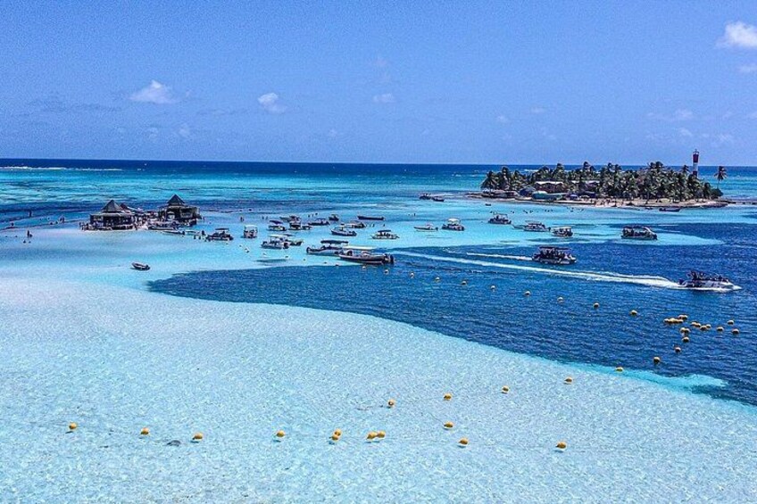 A tropical beach with clear turquoise waters, small boats, and overwater bungalows. 3