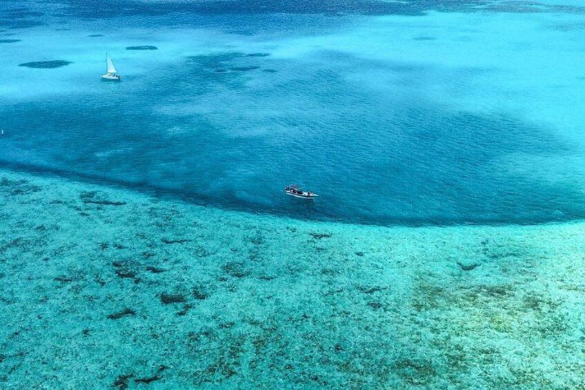 A clear blue sea with a sailboat and a small boat. 2