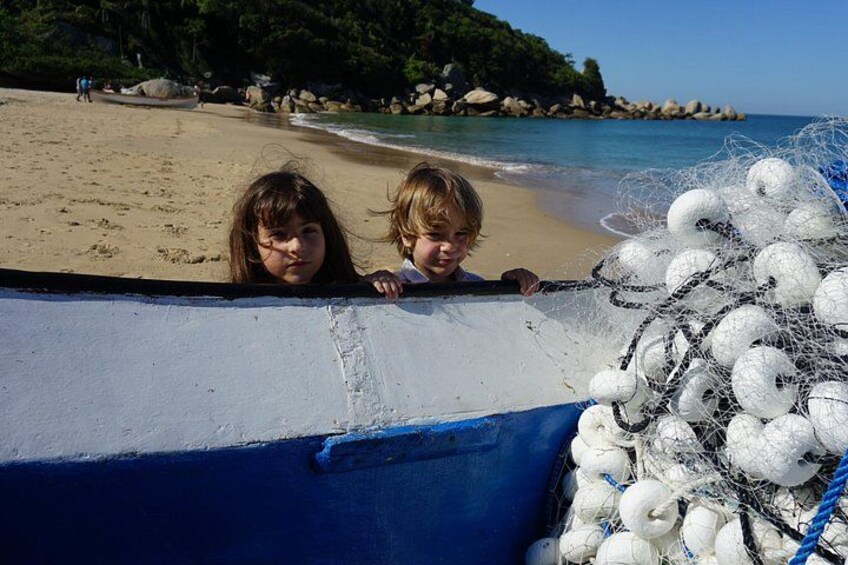 Two children on a beach, a boat with fishing nets, and a rocky shoreline. 2