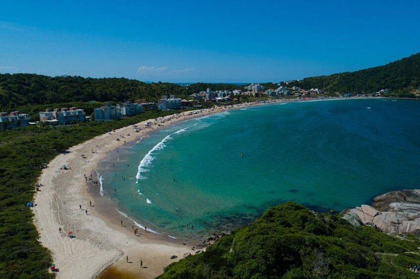 A coastal landscape with a sandy beach, clear turquoise waters, and a backdrop of hills and buildings. 5