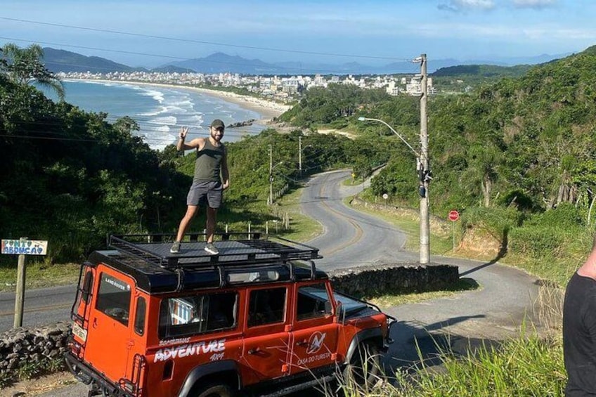 A red Jeep with 'ADVENTURE' written on it, parked on a road with a person standing on top. 1