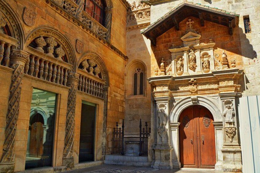 A historic building with ornate stonework, a large wooden door, and a balcony with railings. 4