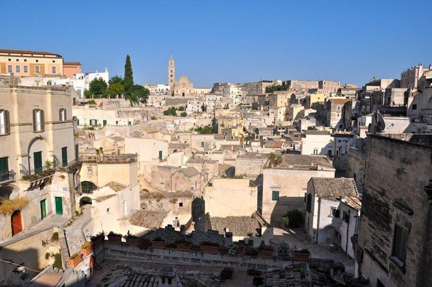 Una zona urbana densamente popolata con edifici storici, un campanile di chiesa in evidenza e un cielo azzurro. 2