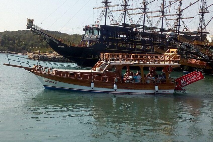 Een houten boot met passagiers, afgemeerd in de buurt van een groter schip. 5