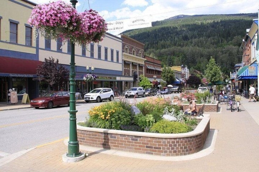A town square with a flower bed, a green lamppost, and buildings with storefronts. 2