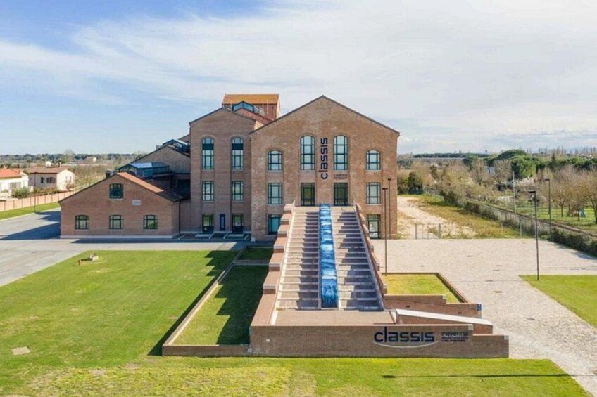 Een groot, bakstenen gebouw met een trap die naar de ingang leidt, omgeven door een verzorgd gazon en een heldere lucht. 1