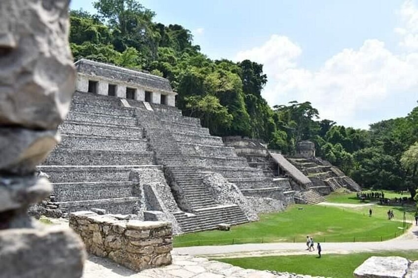 En stor, gammel pyramide med flere niveauer, omgivet af frodig vegetation og en klar himmel. 5