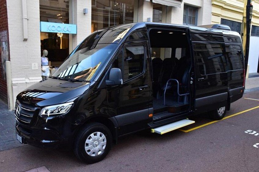 A black van parked on a city street with a storefront in the background. 2