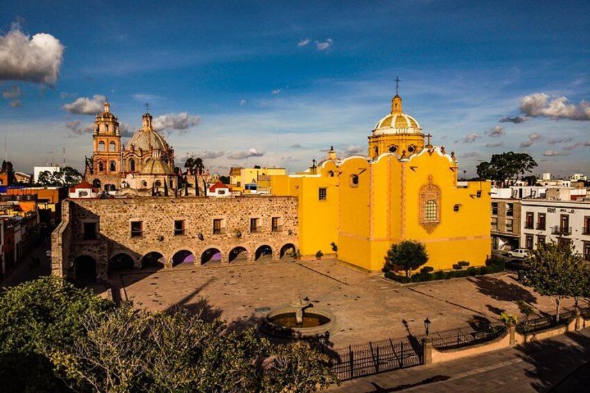 Un edificio de estilo colonial amarillo con una cúpula, un campanario y un patio con arcos. 3