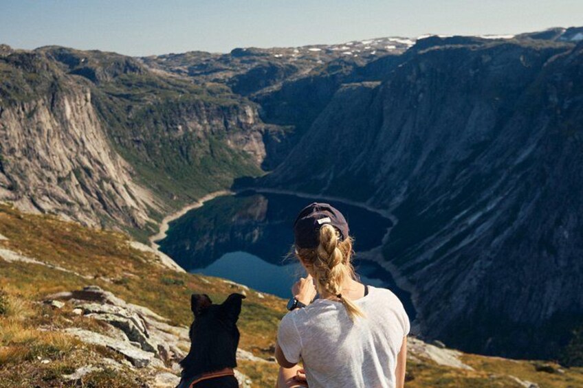 Een persoon en een hond op een bergpad met uitzicht op een vallei met steile kliffen en een meer. 3