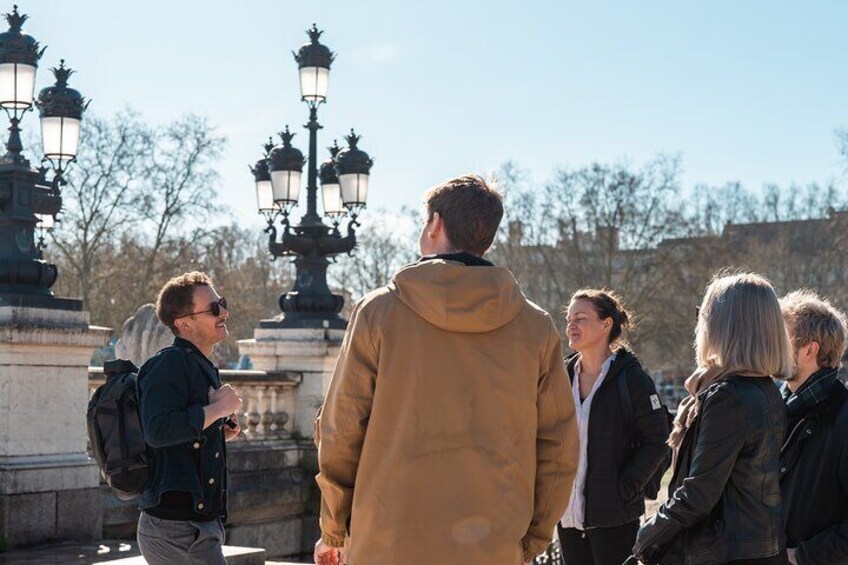 A group of people standing outdoors near a historic building with ornate street lamps. 3
