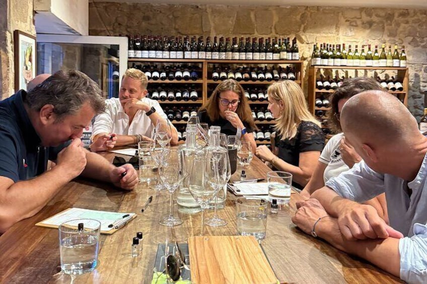 A group of people tasting wine at a table with wine glasses and bottles. 5