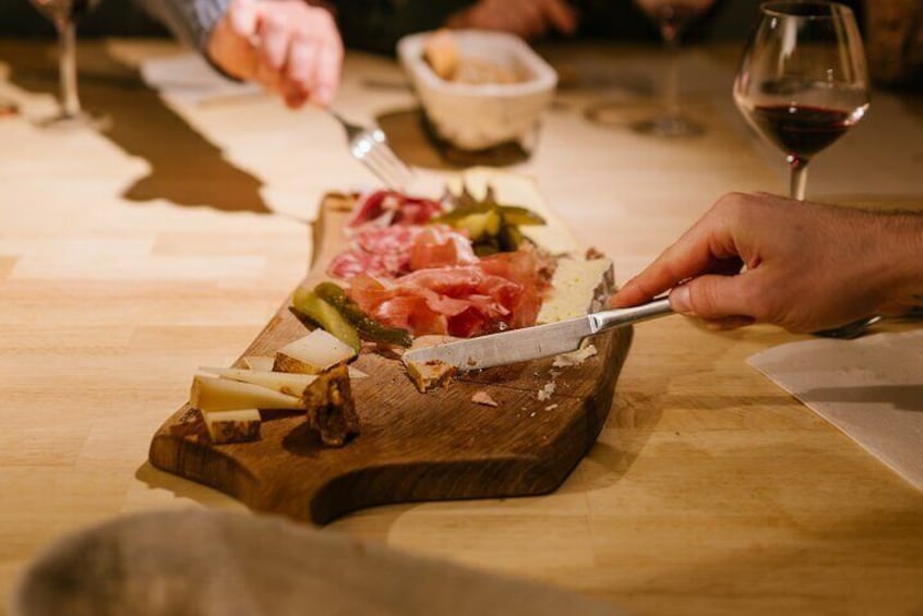 A person cutting a wooden board with various meats and cheeses. 2
