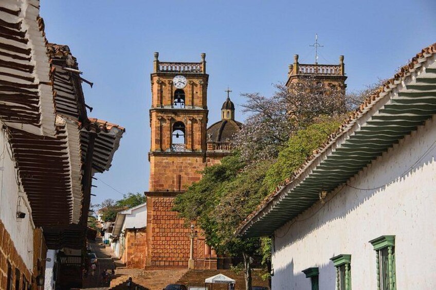 A narrow street with a church tower, a bell tower, and a building with a green window. 2