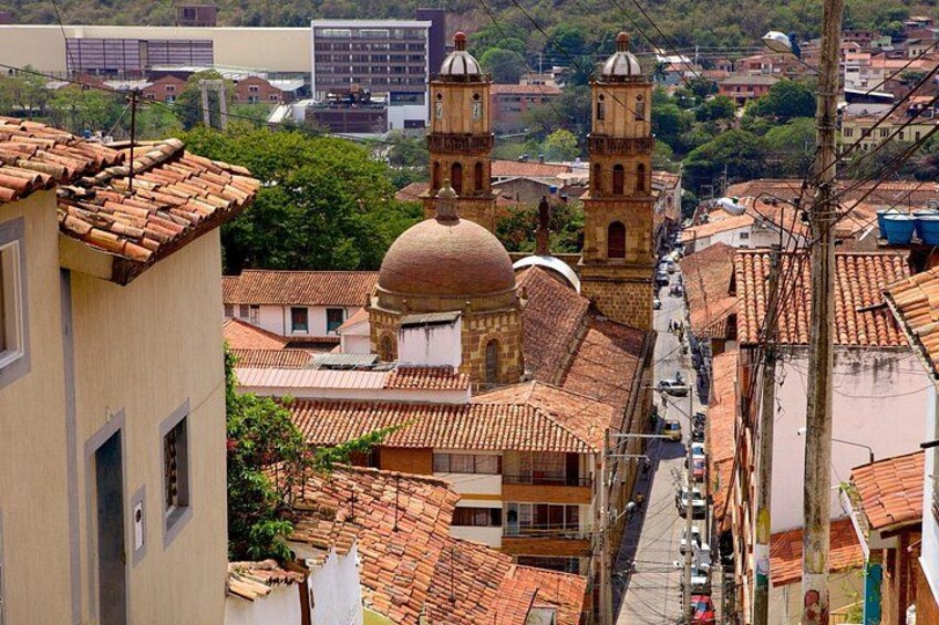 A cityscape with terracotta-roofed buildings, a prominent church with two domes, and a tower. 3