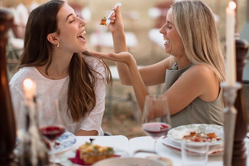 Twee personen dineren aan een buitentafel, met kaarsen, borden eten en wijnglazen. 4