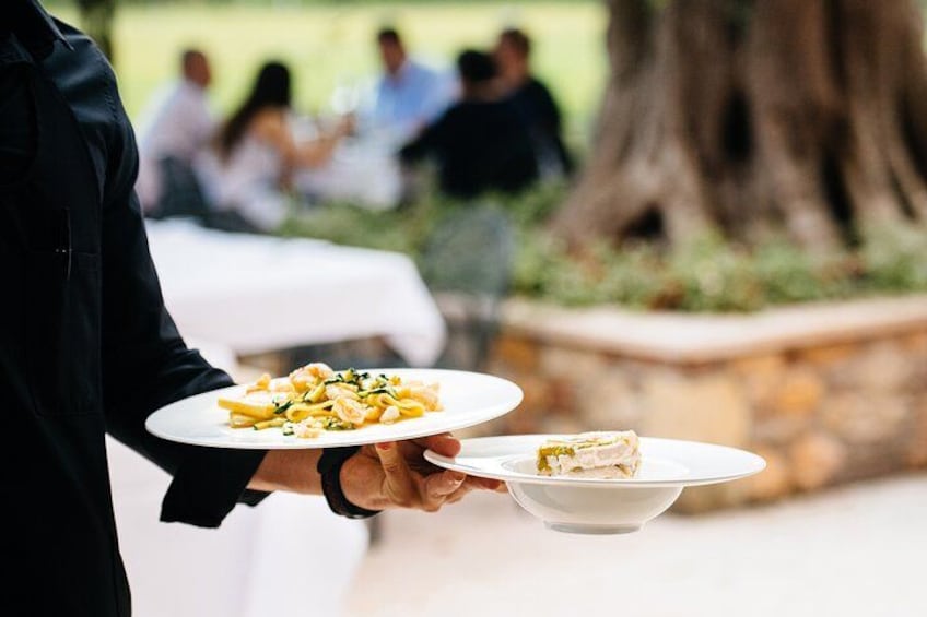 A person holding a plate of pasta and a bowl of salad. 4
