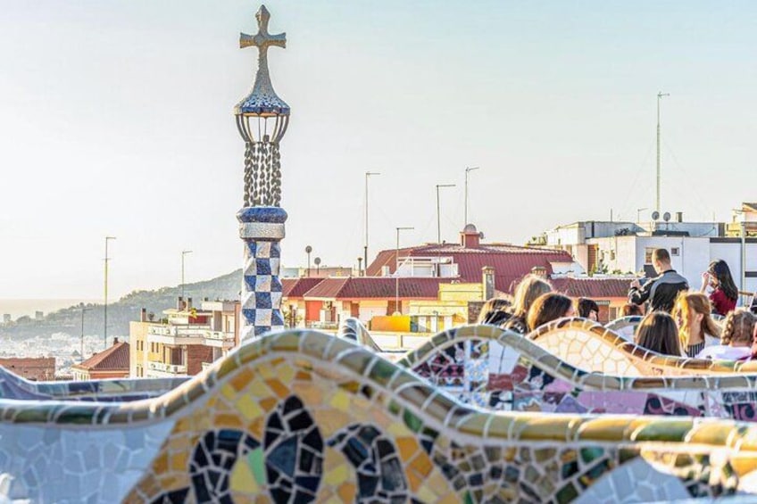 A tiled walkway with a mosaic pattern, a tower with a cross, and buildings in the background. 3