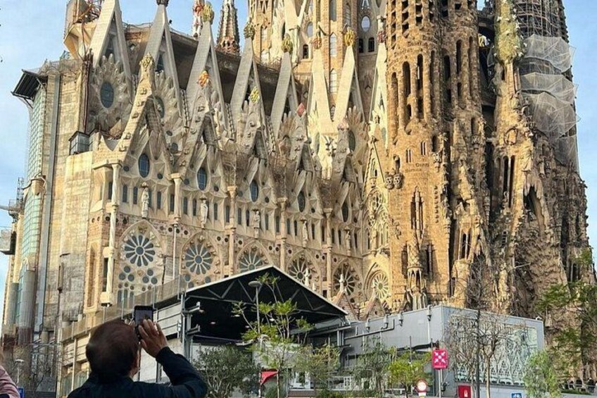 Ein großes, verziertes Gebäude mit aufwendiger Architektur, eine Person macht ein Foto, und ein modernes Bauwerk im Vordergrund. 4