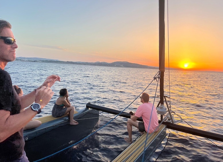 Three people on a boat deck at sunset, with the sun setting over the water. 1