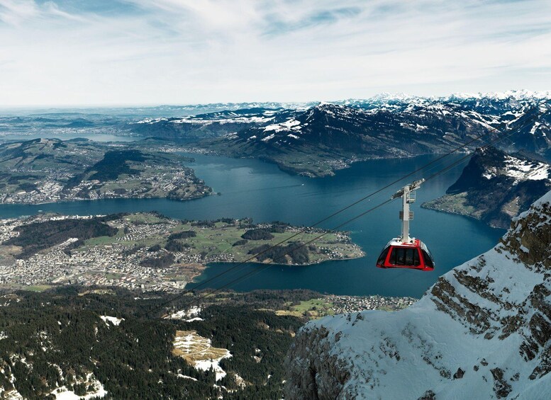 A cable car ascending a mountain with a lake and town below. 1