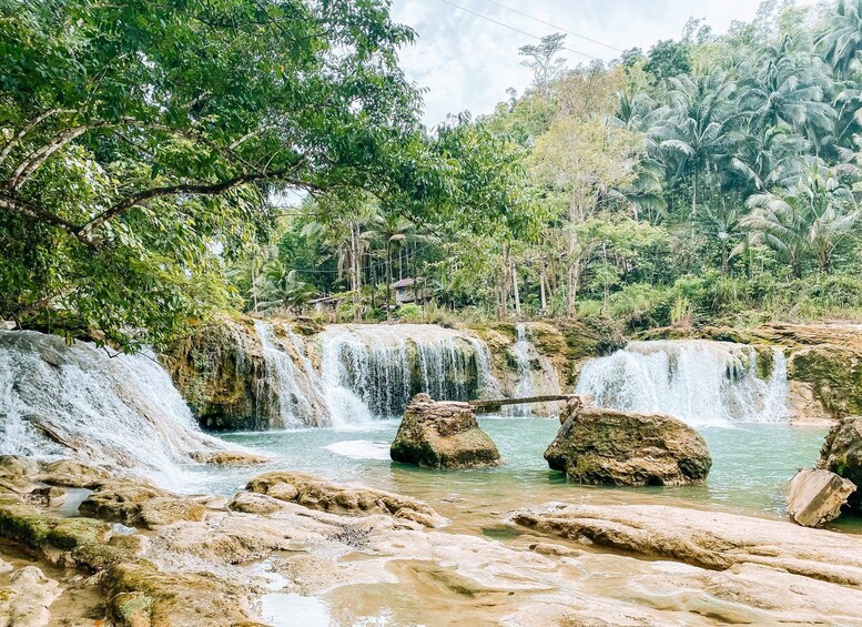 A waterfall cascading over rocks into a clear pool, surrounded by lush greenery and trees. 3