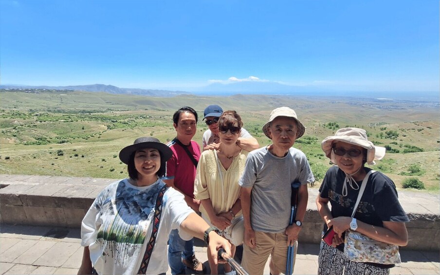 A group of people standing on a stone platform overlooking a vast landscape with rolling hills and distant mountains. 2