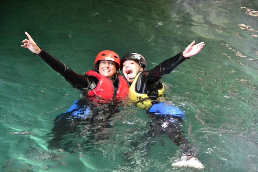Two people in water with life jackets and helmets, one pointing upwards. 3