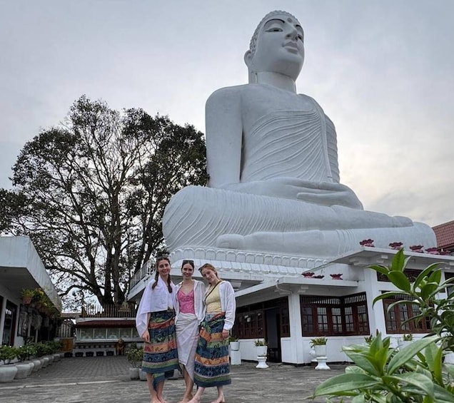 A large white Buddha statue, three people standing in front, and a building with a tiled roof. 3
