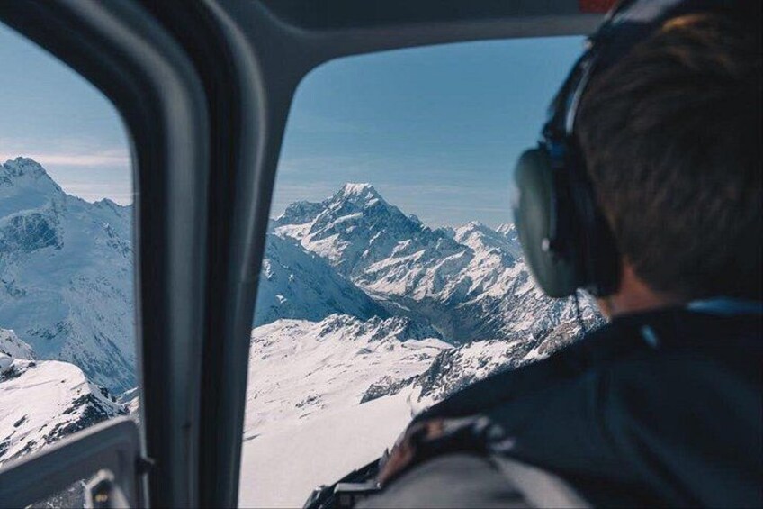 A person wearing headphones, looking out of a helicopter window at snow-covered mountains. 2