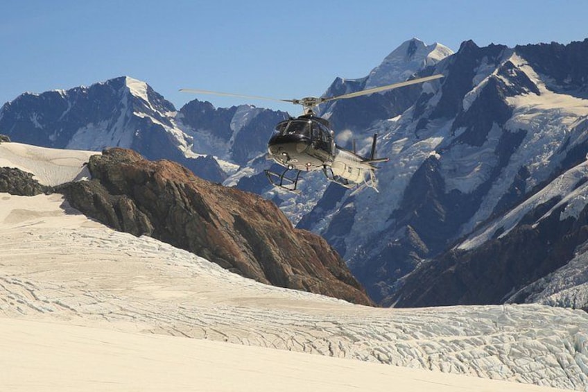 A helicopter flying over a snowy mountain landscape with rocky outcrops. 1