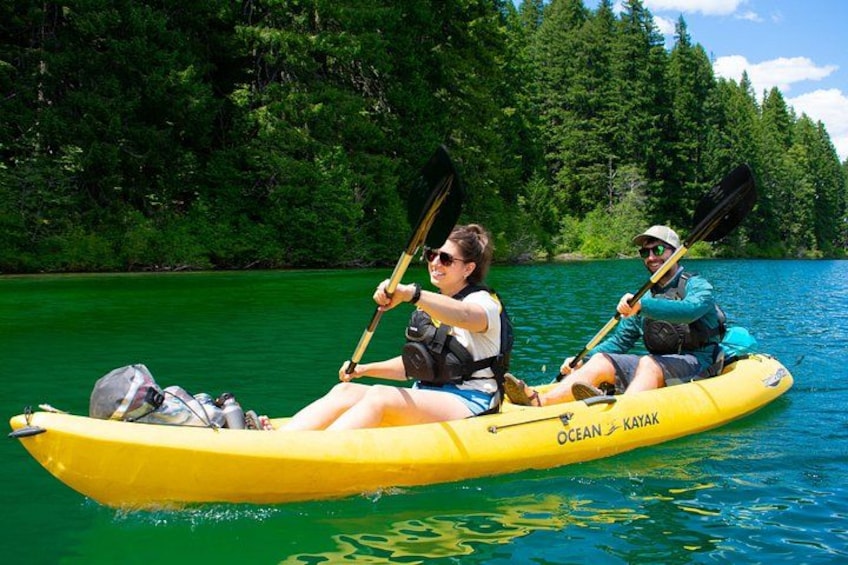 Dos personas en kayak amarillo, con la inscripción 'OCEAN KAYAK', en un lago rodeado de bosque. 2