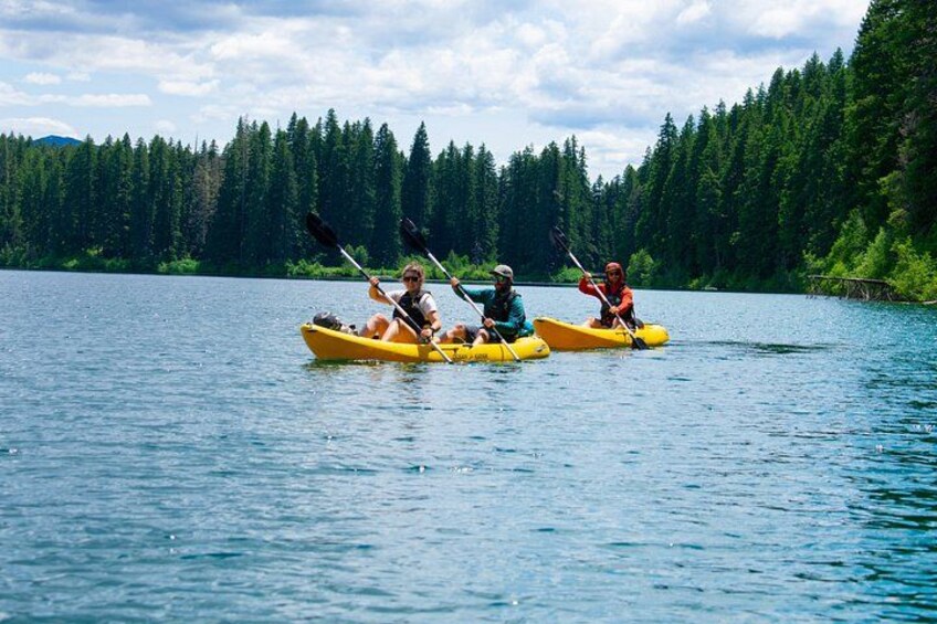 Tres personas kayakendo en un lago tranquilo bordeado por un bosque denso. 4
