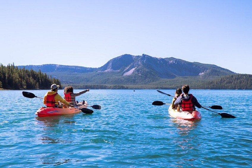 Tres personas remando en kayak en un lago tranquilo con montañas al fondo. 3
