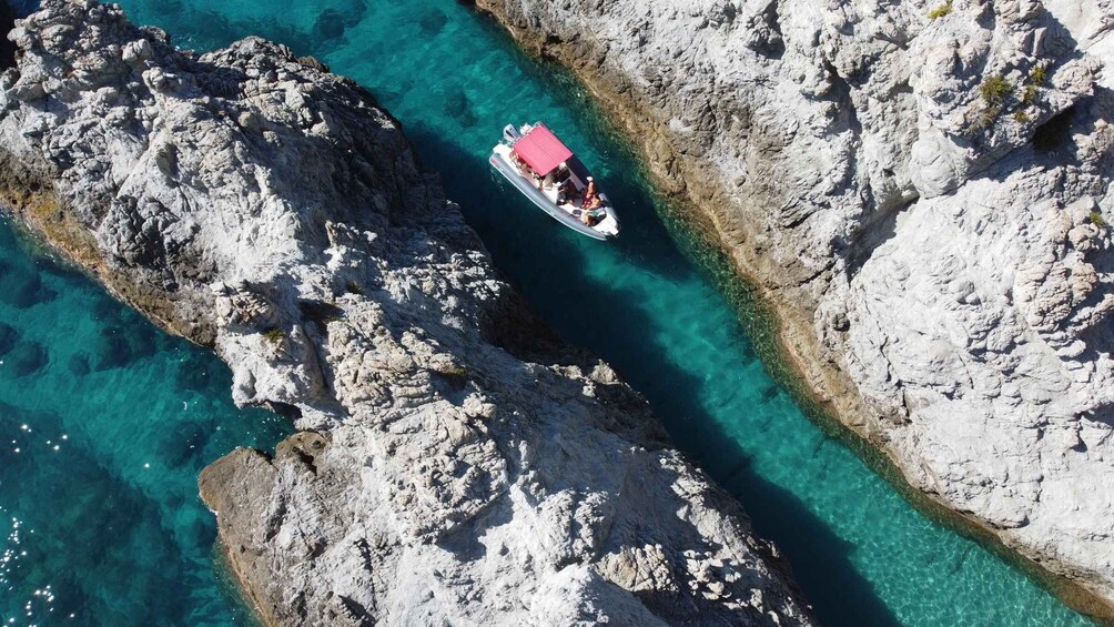 An aerial view of a rocky coastline with clear turquoise waters and a small boat with a red roof. 2