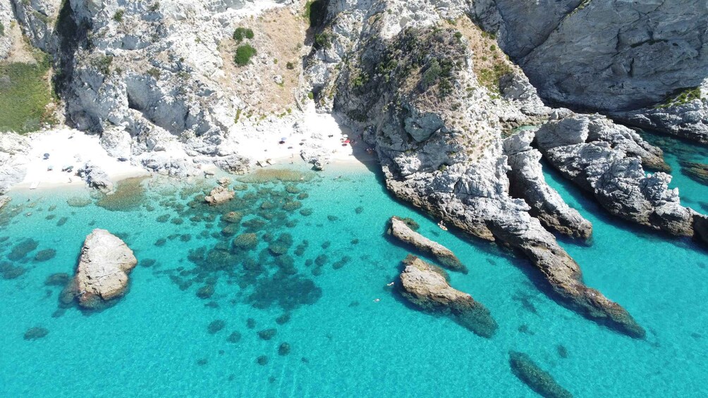A coastal landscape with clear turquoise waters, rocky formations, and a sandy beach. 3