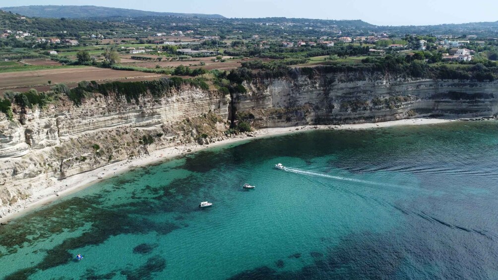 A coastal landscape with cliffs, a beach, and boats on the water. 4