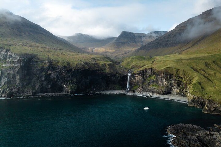 A coastal landscape with a waterfall, a small boat, and rugged cliffs. 2