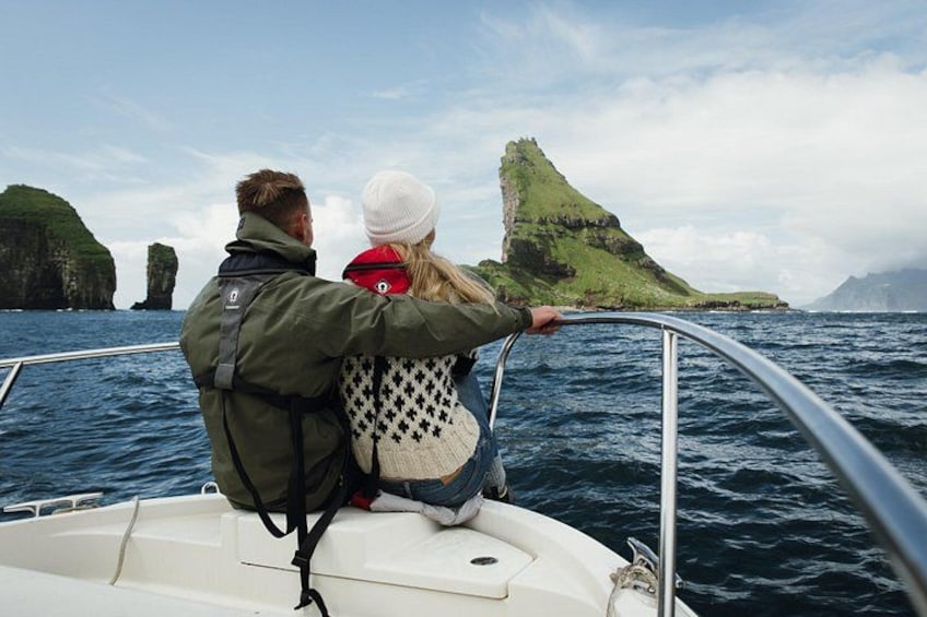 A couple on a boat, facing a green cliff by the sea. 3