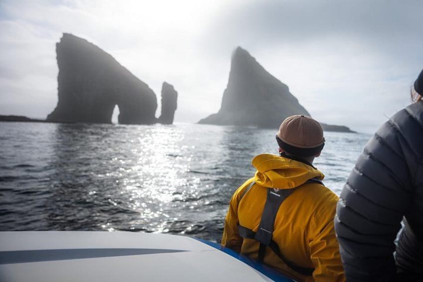 A boat with two people wearing jackets, a rocky coastline with large rock formations, and a calm sea. 4