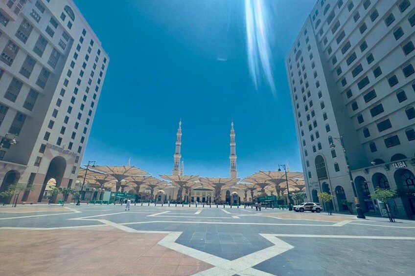 Ein Stadtplatz mit zwei hohen Gebäuden, einer Moschee mit zwei Minaretten und blauem Himmel. 1