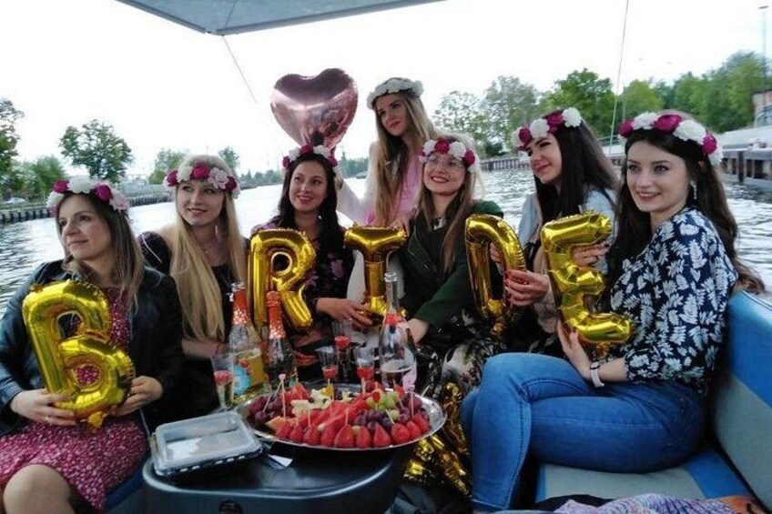 A group of people on a boat with 'BRIDE' balloons and a cake. 5
