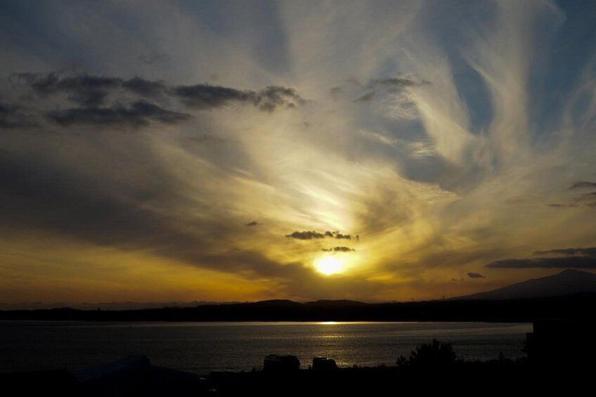 Un coucher de soleil sur une étendue d’eau, avec des nuages et les silhouettes de terres au premier plan. 5