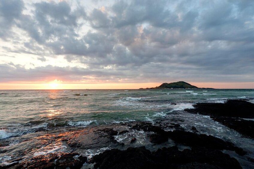 Un paysage côtier avec des vagues qui s’écrasent sur des rochers, une île lointaine et un coucher de soleil. 4