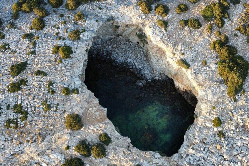 A large sinkhole surrounded by rocky terrain and sparse vegetation. 3