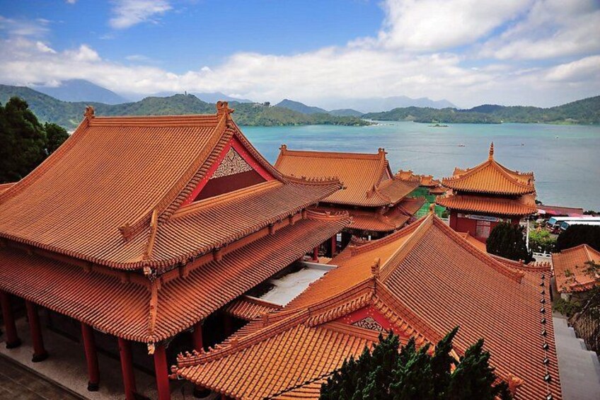 Traditional Chinese architecture with tiled roofs, a body of water, and mountains in the background. 5