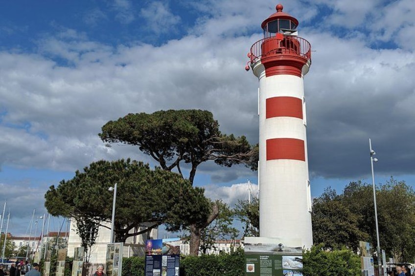 A tall lighthouse with red and white stripes, surrounded by trees and a cloudy sky. 2
