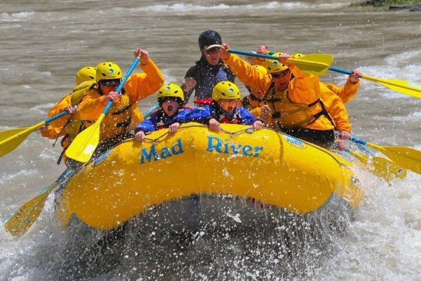 Een groep mensen in een gele raft met de tekst 'Mad River' die door een rivier peddelt. 5