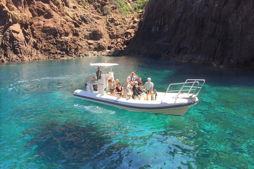 A boat with passengers on a clear blue sea, surrounded by rocky cliffs. 5